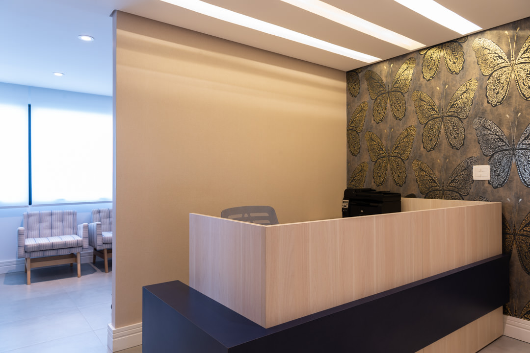 Recepção com balcão em madeira clara e sala de espera ao fundo, em projeto de interiores corporativo da Intetto