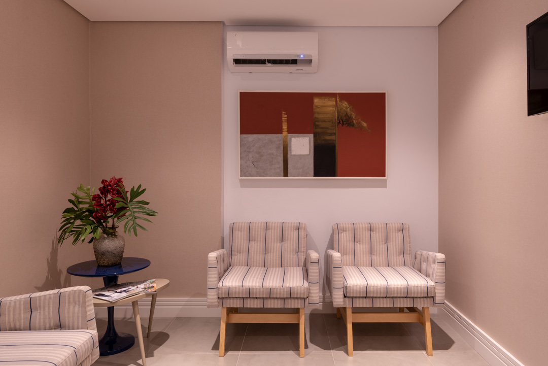 Sala de espera com duas poltronas listradas, mesa lateral azul e quadro na parede, em projeto de interiores corporativo da Intetto